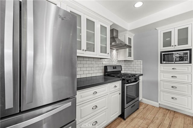 kitchen featuring appliances with stainless steel finishes, tasteful backsplash, white cabinets, wall chimney exhaust hood, and light hardwood / wood-style flooring