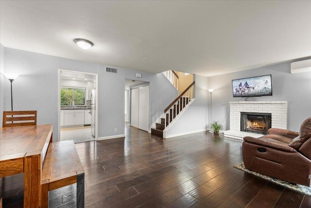 living room featuring a wall unit AC, a fireplace, and dark hardwood / wood-style flooring