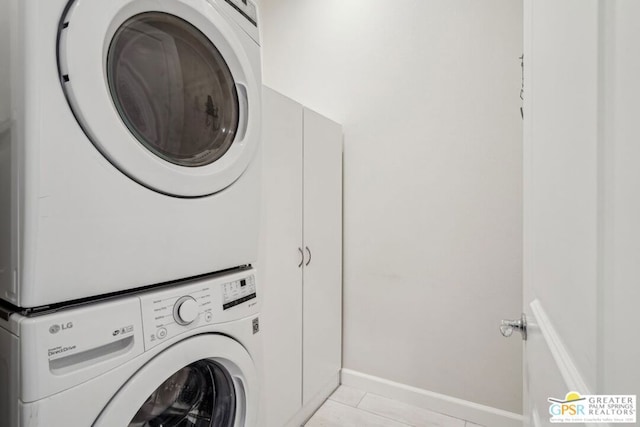 washroom featuring stacked washer and dryer, light tile patterned floors, and cabinets