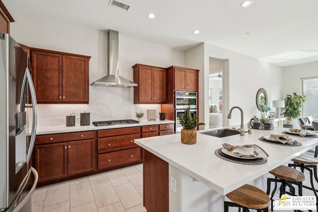 kitchen featuring a kitchen island with sink, sink, wall chimney exhaust hood, and appliances with stainless steel finishes