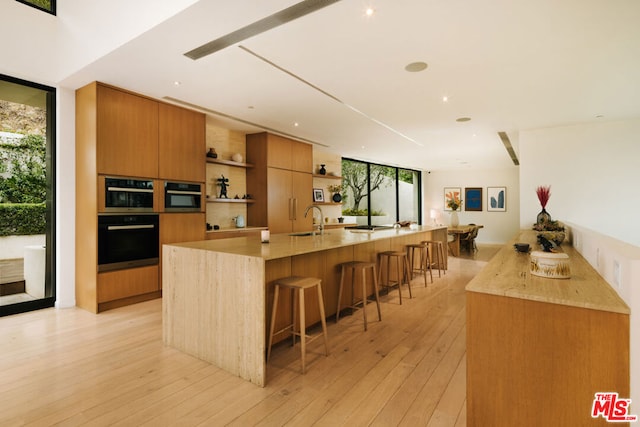 kitchen featuring sink, light hardwood / wood-style flooring, a wall of windows, a kitchen breakfast bar, and a spacious island