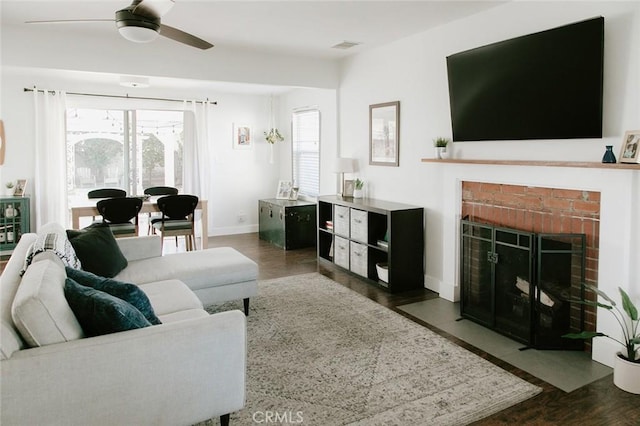 living room featuring a brick fireplace, dark wood-type flooring, and ceiling fan