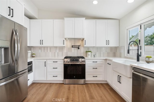 kitchen with tasteful backsplash, vaulted ceiling, stainless steel appliances, light hardwood / wood-style floors, and white cabinets