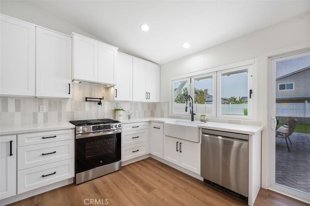 kitchen with appliances with stainless steel finishes, tasteful backsplash, white cabinetry, sink, and light hardwood / wood-style floors