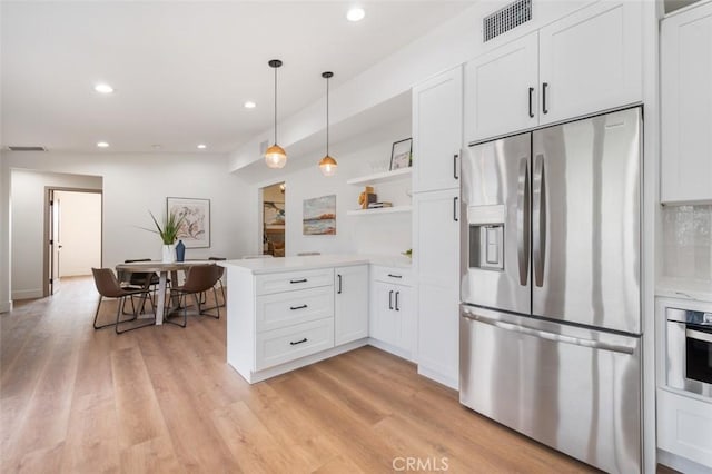 kitchen featuring appliances with stainless steel finishes, white cabinets, hanging light fixtures, kitchen peninsula, and light hardwood / wood-style flooring