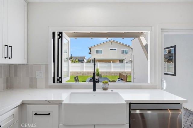 kitchen with sink, backsplash, light stone countertops, white cabinets, and stainless steel dishwasher