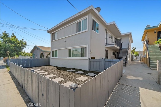 back of house with a fenced backyard, stairs, and stucco siding