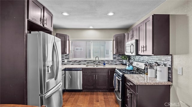 kitchen featuring sink, dark wood-type flooring, stainless steel appliances, light stone counters, and tasteful backsplash