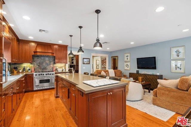 kitchen featuring sink, high end stainless steel range oven, an island with sink, custom range hood, and decorative light fixtures