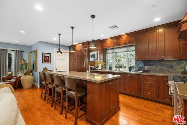 kitchen with pendant lighting, sink, a kitchen breakfast bar, built in appliances, and a center island with sink