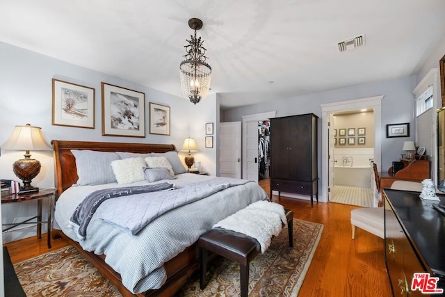 bedroom with ensuite bathroom, a chandelier, dark hardwood / wood-style flooring, a walk in closet, and a closet