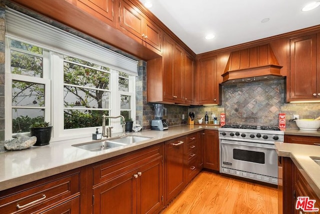 kitchen with sink, custom exhaust hood, tasteful backsplash, luxury stove, and light wood-type flooring