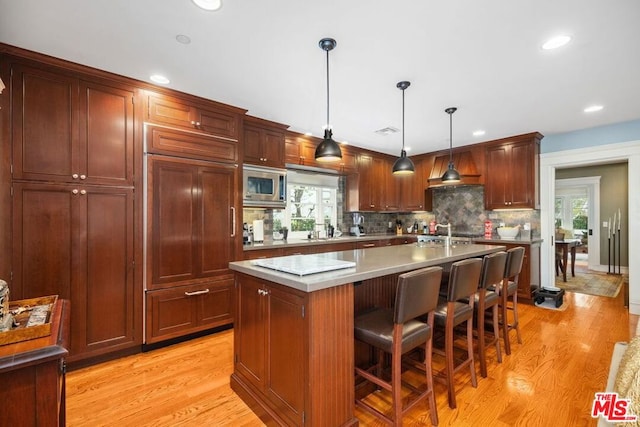 kitchen with a breakfast bar area, hanging light fixtures, built in appliances, a healthy amount of sunlight, and a center island with sink