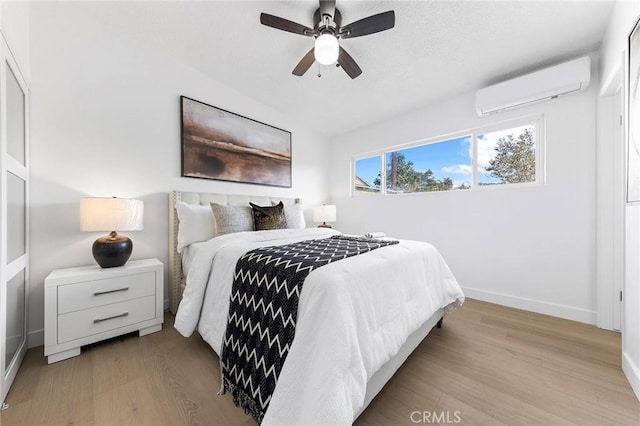 bedroom featuring ceiling fan, light hardwood / wood-style flooring, and a wall mounted AC