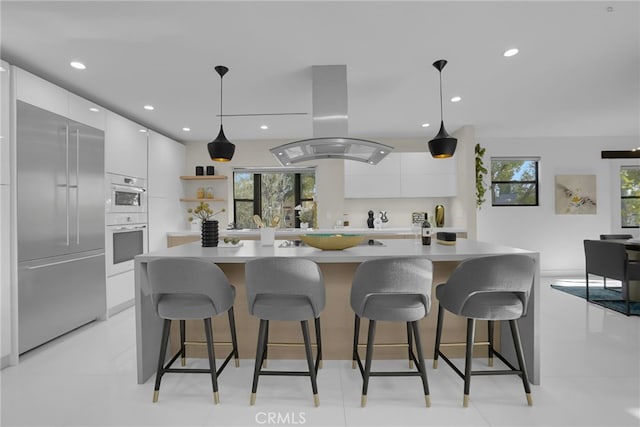 kitchen featuring decorative light fixtures, white cabinetry, stainless steel built in refrigerator, island exhaust hood, and a kitchen island with sink