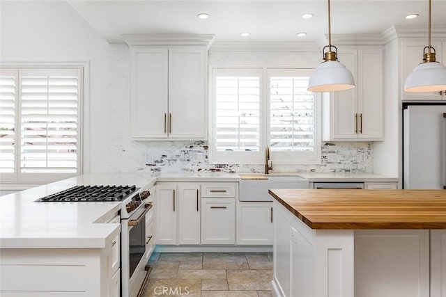 kitchen with sink, gas range, white cabinetry, decorative light fixtures, and a wealth of natural light