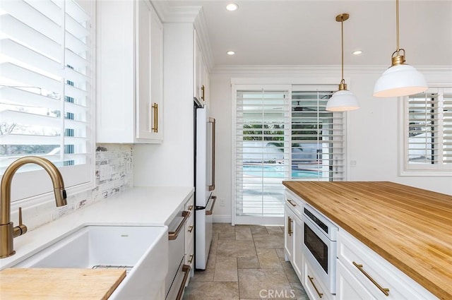 kitchen with sink, white cabinetry, hanging light fixtures, backsplash, and stainless steel microwave