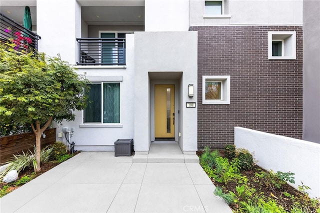 property entrance featuring brick siding, fence, a balcony, and stucco siding