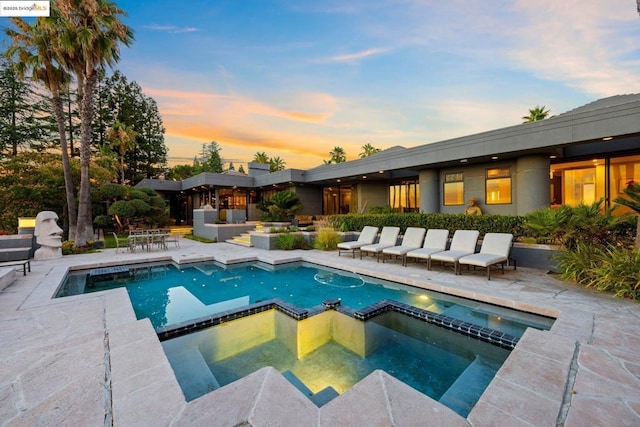 pool at dusk featuring an in ground hot tub and a patio