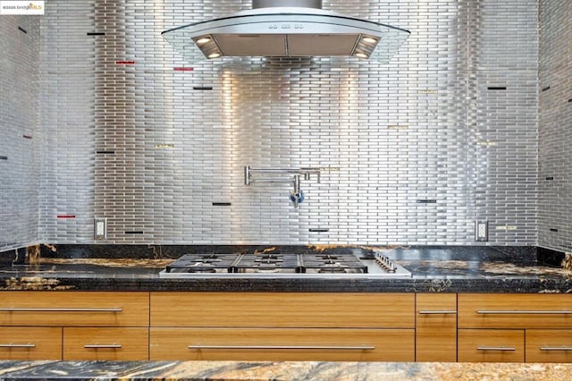 interior space featuring stainless steel gas stovetop, exhaust hood, dark stone countertops, and backsplash