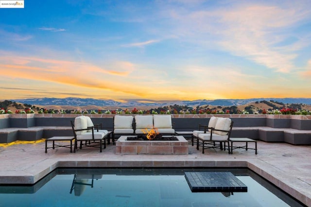 pool at dusk with a mountain view, a patio, and an outdoor living space with a fire pit