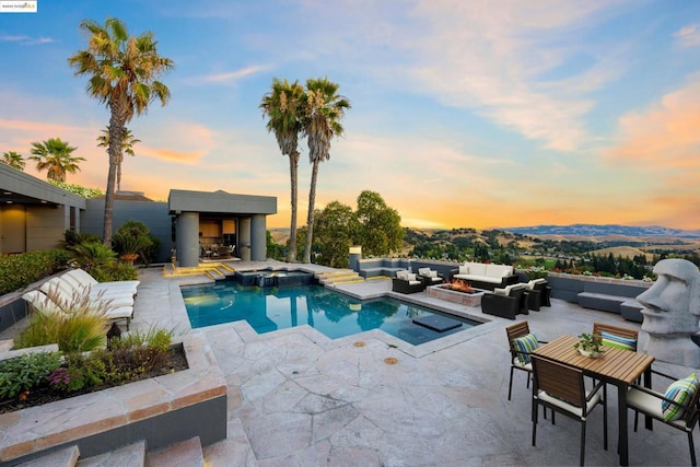 pool at dusk featuring an outdoor living space with a fireplace, a mountain view, and a patio