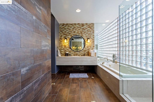 bathroom with tiled tub, wood-type flooring, and tile walls