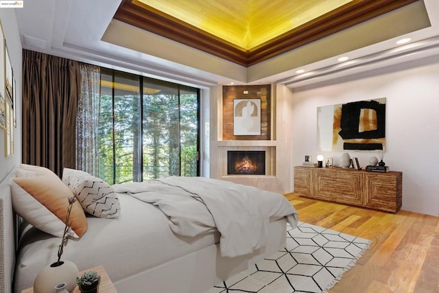 bedroom with a fireplace, wood-type flooring, and a raised ceiling