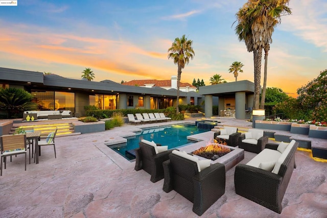 pool at dusk with an outdoor living space with a fire pit and a patio area