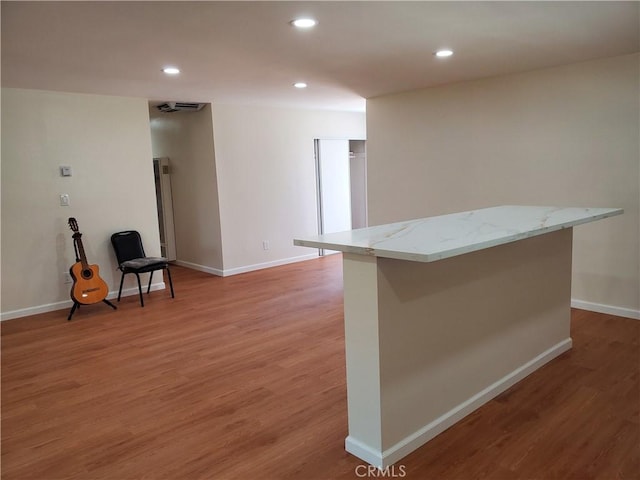 kitchen with hardwood / wood-style flooring, light stone countertops, and a kitchen island