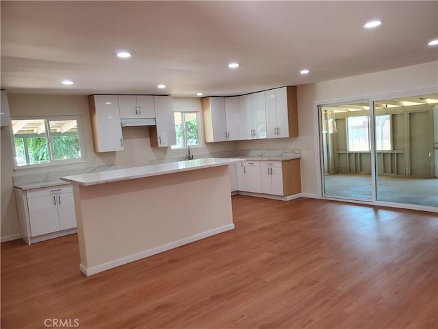 kitchen with white cabinetry, sink, a center island, and light hardwood / wood-style floors