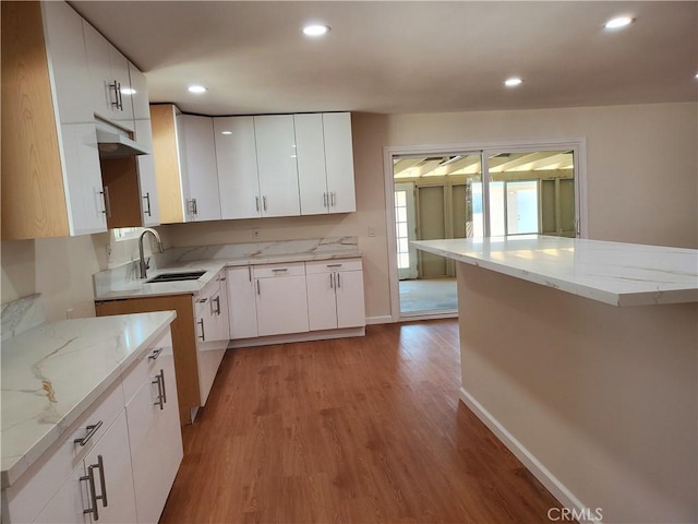 kitchen featuring white cabinetry, sink, light stone counters, and light hardwood / wood-style flooring