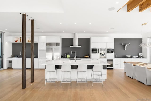 kitchen with pendant lighting, wall chimney range hood, a breakfast bar area, appliances with stainless steel finishes, and white cabinetry