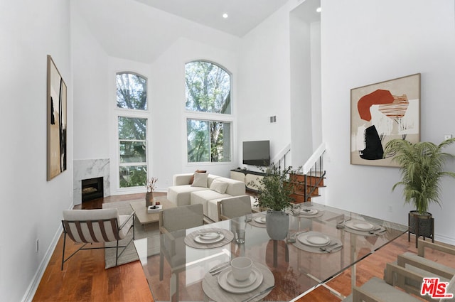 living room with a towering ceiling, wood-type flooring, and a high end fireplace