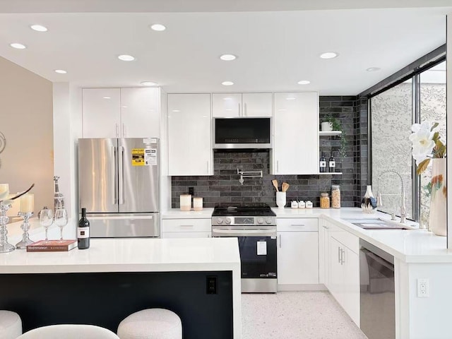 kitchen with sink, a breakfast bar, appliances with stainless steel finishes, white cabinetry, and tasteful backsplash