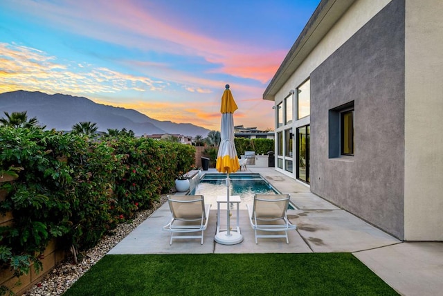 pool at dusk with a mountain view, a yard, and a patio area