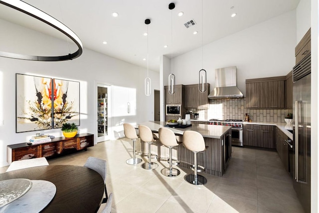 kitchen featuring dark brown cabinets, stainless steel range, a kitchen island, built in microwave, and wall chimney exhaust hood