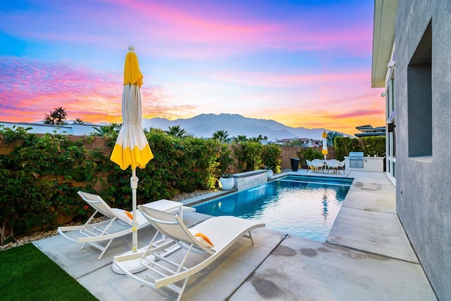 pool at dusk featuring area for grilling, a mountain view, and a patio area