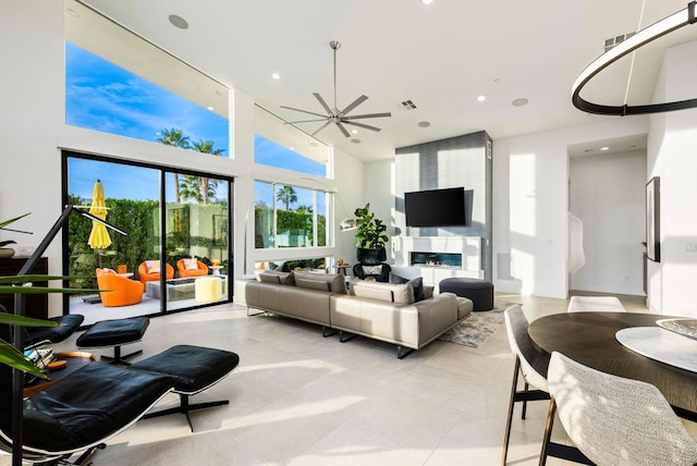 living room with a large fireplace, ceiling fan, and a high ceiling