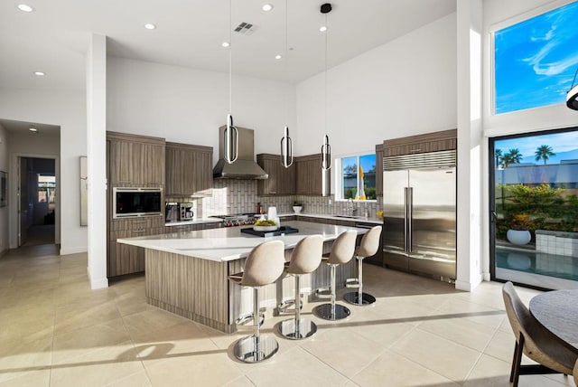 kitchen featuring wall chimney range hood, a breakfast bar area, hanging light fixtures, built in appliances, and a kitchen island