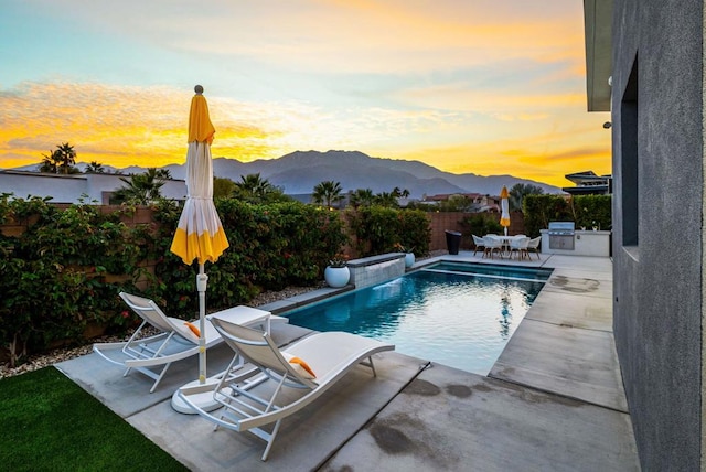 pool at dusk with exterior kitchen, a mountain view, and a patio