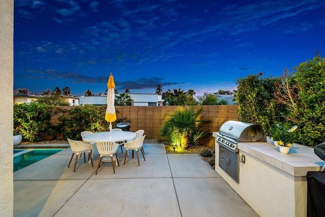 patio terrace at dusk featuring a fenced in pool, an outdoor kitchen, and grilling area