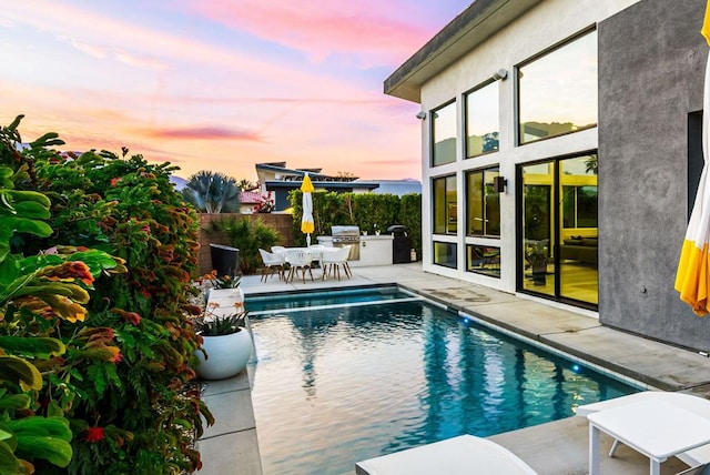 pool at dusk featuring a grill, a patio area, and exterior kitchen