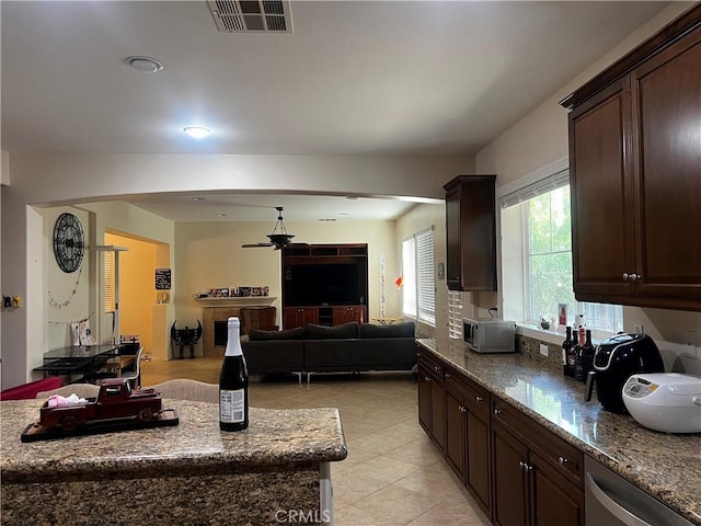 kitchen with stone counters, stainless steel dishwasher, light tile patterned floors, ceiling fan, and dark brown cabinets