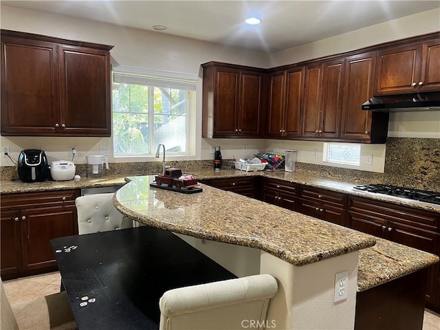 kitchen featuring a breakfast bar, backsplash, a center island, light stone counters, and gas stovetop