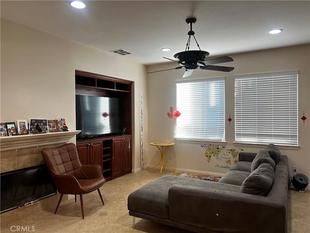 tiled living room with a tiled fireplace and ceiling fan