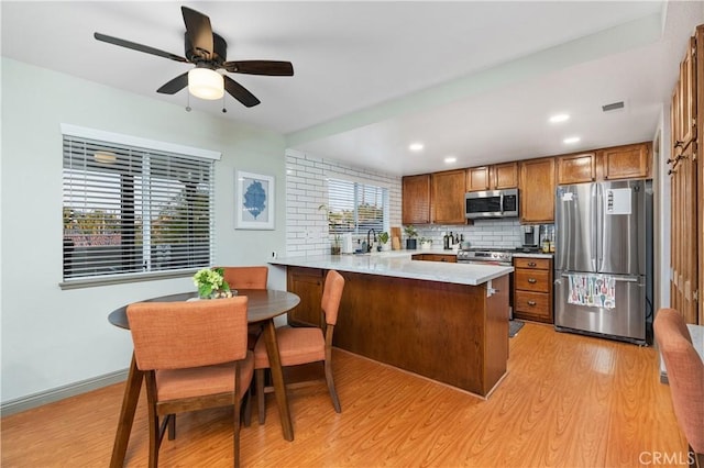 kitchen with light hardwood / wood-style flooring, ceiling fan, appliances with stainless steel finishes, decorative backsplash, and kitchen peninsula