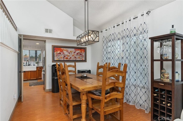 dining room with sink, vaulted ceiling, a chandelier, and light wood-type flooring