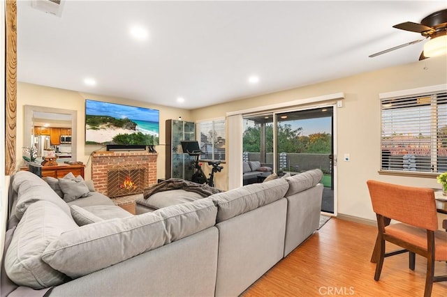 living room featuring a brick fireplace, light hardwood / wood-style floors, and ceiling fan