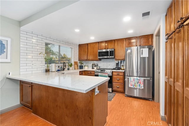 kitchen featuring sink, light wood-type flooring, kitchen peninsula, stainless steel appliances, and backsplash